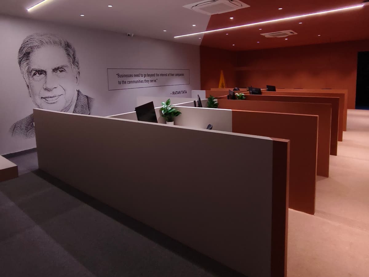 The open-plan floor seen along its length, with partitioned desks, strip lighting in the ceiling and the Ratan Tata mural on the far wall